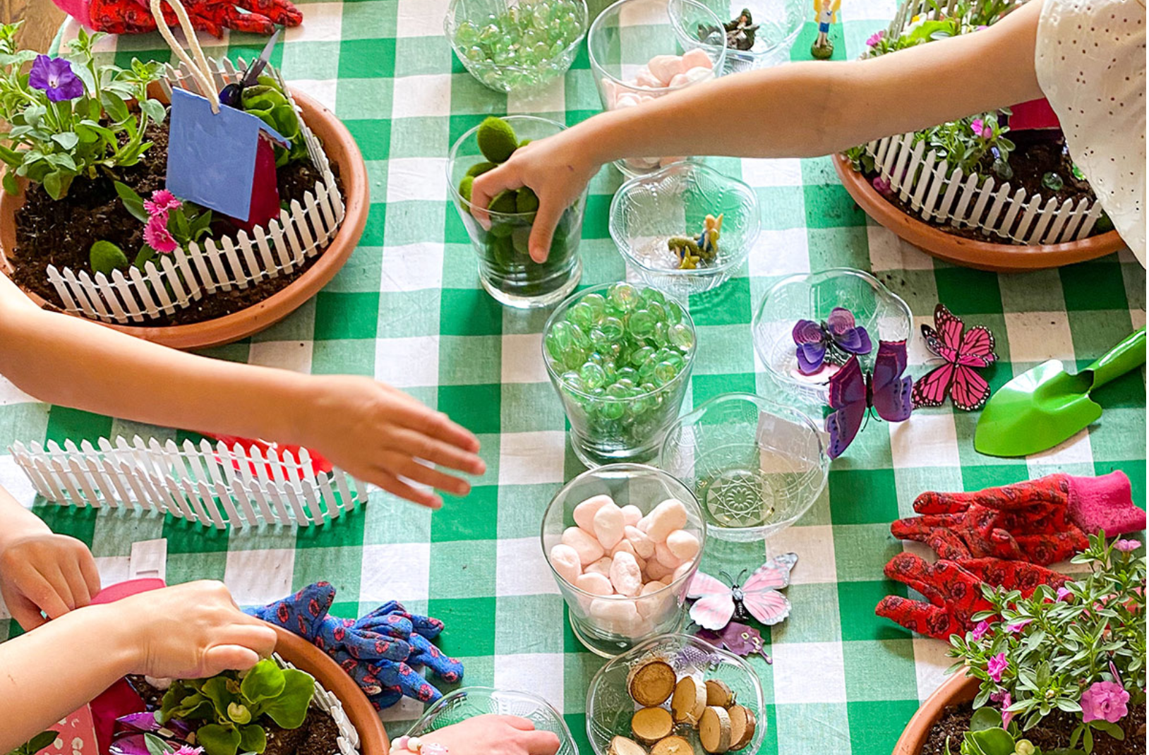 Hands planting moss and small plants inside a glass terrarium at a party table