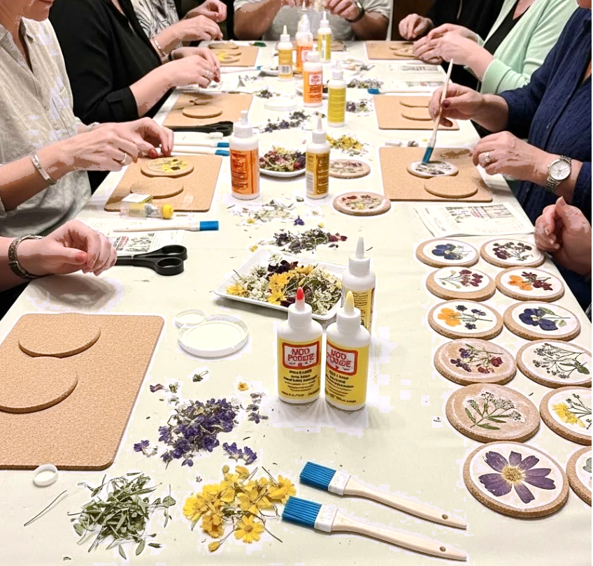 A group at a long table decorating cork coasters with pressed flowers and Mod Podge